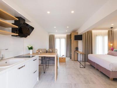 Helles, modernes Studio mit Küchenzeile, Esstisch, Bett, Fernseher und großen Fenstern mit Vorhängen.