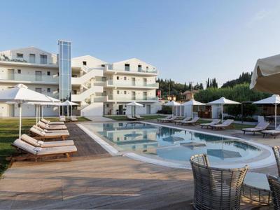 Moderner Hotelpool mit Liegestühlen, Sonnenschirmen und weißem Gebäude im Hintergrund bei klarem Himmel.