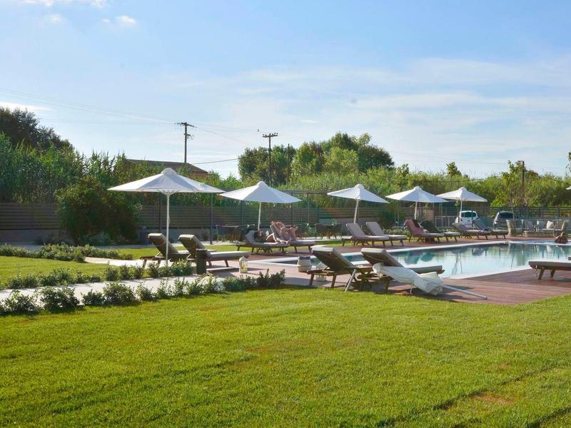 Grüner Rasen mit Pool, Holzdeck und weißen Sonnenschirmen an einem sonnigen Tag.