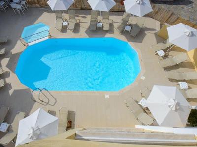 Ovaler Pool mit klarem blauem Wasser, umgeben von weißen Sonnenschirmen und Liegestühlen.