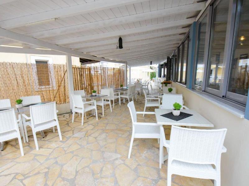 Terrasse couverte avec des chaises blanches et des tables le long des fenêtres d'un bâtiment.