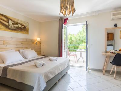 Camera d'hotel luminosa con letto matrimoniale, tavolo e sedia, accesso al balcone con vista verde.