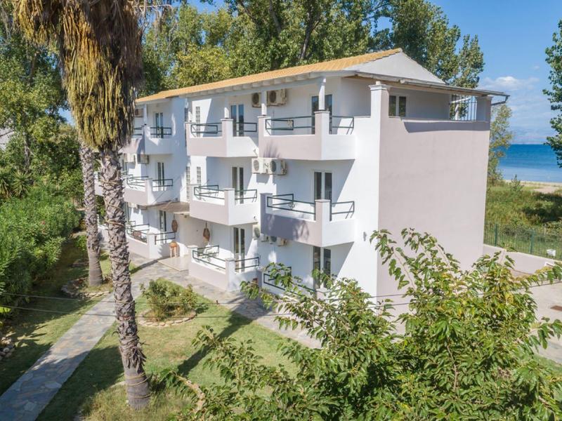 Třípatrový hotel s balkónovými pokoji v zeleném prostředí blízko pláže.