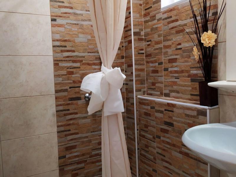 Badezimmer mit beiger Duschvorhang, braun-beigen Fliesen und weißem Waschbecken.