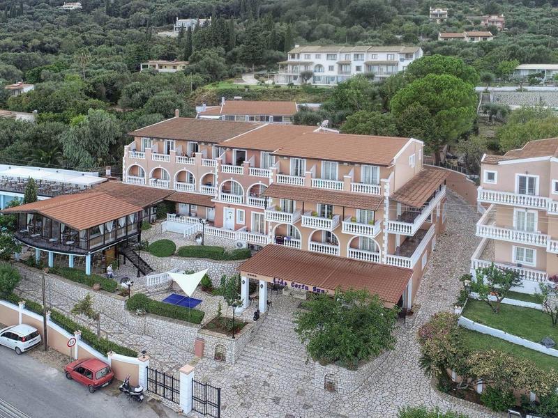 Hôtel à plusieurs étages avec toit en terre cuite, piscine et vue sur des collines boisées.