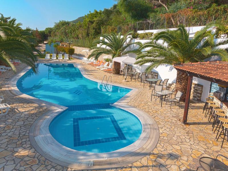 Zone de piscine avec deux piscines reliées, entourée de palmiers et d'un bar voisin.