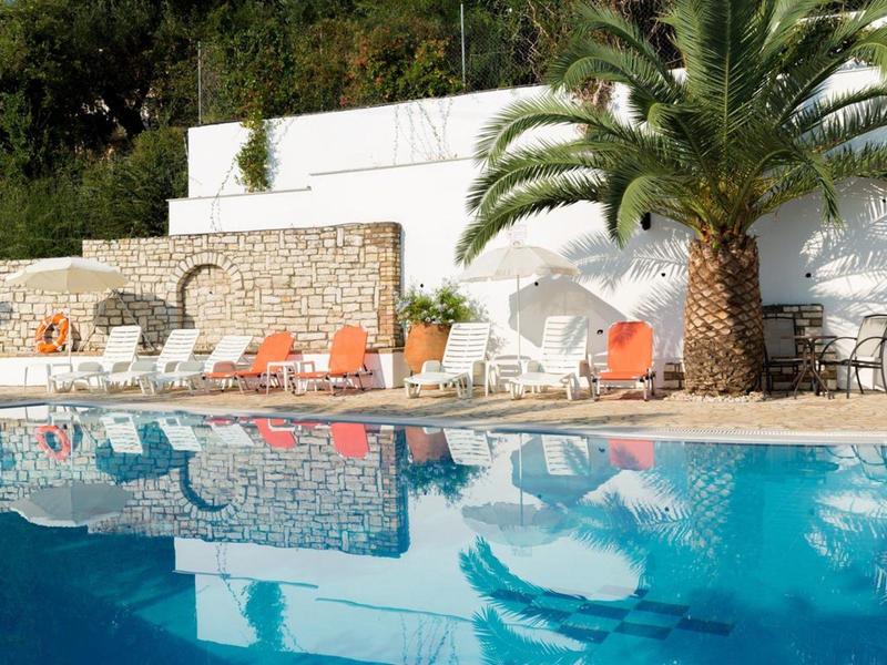 Piscine avec chaises longues et palmiers dans un hôtel par temps ensoleillé.