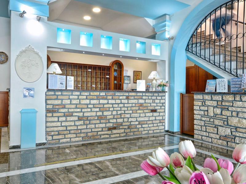 Réception d'hôtel lumineuse avec mur en pierre, fleurs et escalier en arrière-plan.