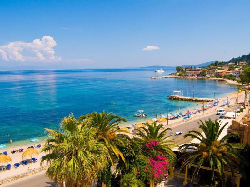 Plage avec eau bleue claire, palmiers et parasols par temps ensoleillé.