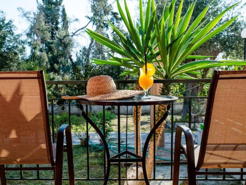 Deux chaises avec table, cocktail tropical et chapeau de soleil sur un balcon avec vue sur les jardins.
