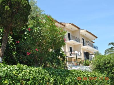 Mehrstöckiges Haus mit weißen Wänden, Balkonen und grünen Pflanzen im sonnigen Garten.