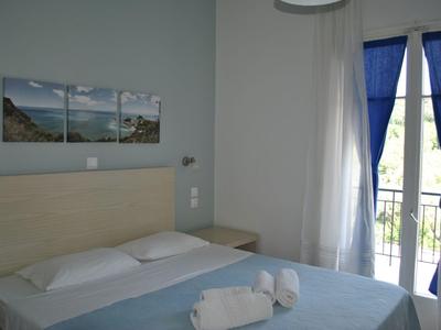 Ein ruhiges Hotelzimmer mit einem Doppelbett, hellen Wänden und einem Balkon mit blauen Vorhängen.