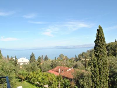 Pohled na zelené stromy, domy s červenými střechami a modrou oblohu u moře.
