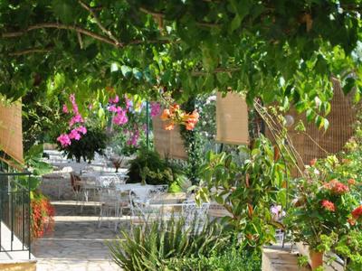 Ein schattiger Gartenbereich mit blühenden Pflanzen und einem Sitzbereich im Hintergrund.
