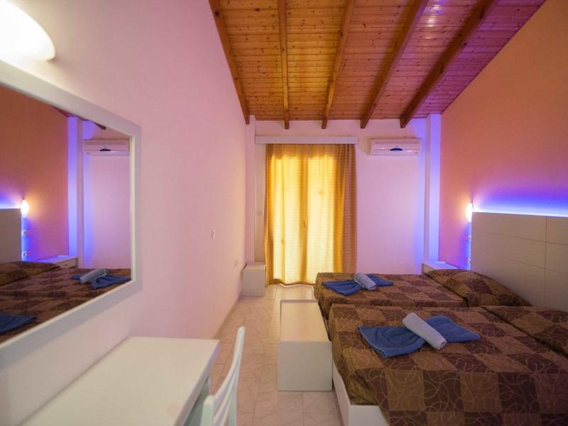 Piccola camera d'hotel con letto matrimoniale, soffitto con travi di legno e illuminazione a LED blu sulle pareti.