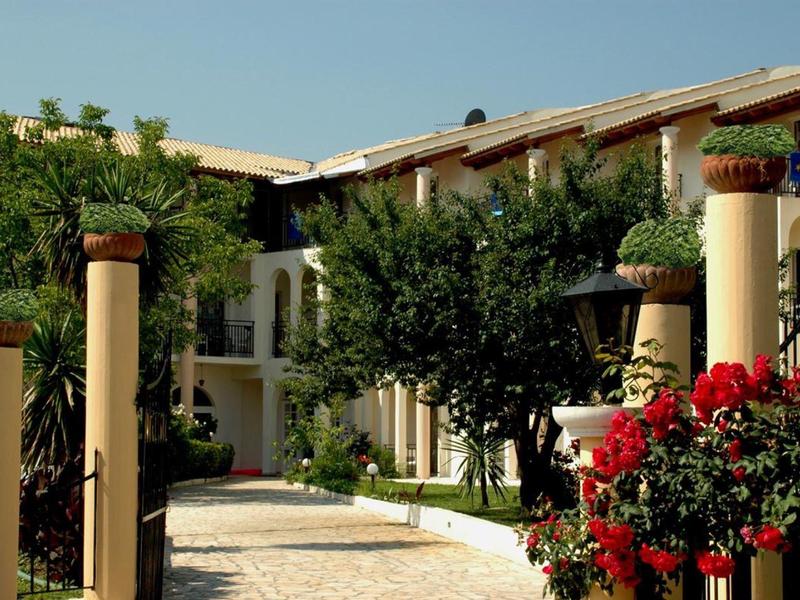 Complesso alberghiero moderno con fiori rossi e colonne lungo un sentiero lastricato.