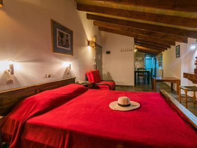 Gezellige hotelkamer met houten plafond, rood bed en stoel, versierd met een hoed.