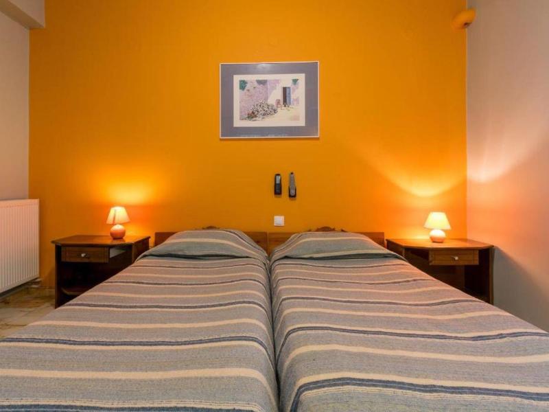 Twee eenpersoonsbedden met gestreepte dekens voor een oranje muur met nachtlampjes