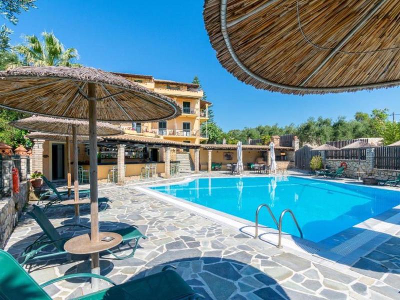 Buitenzwembad met ligstoelen en rieten parasols naast een hotelgebouw.
