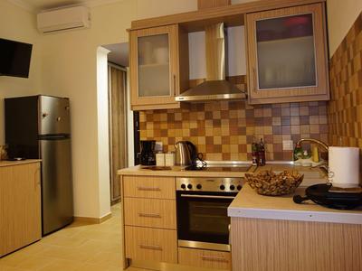 Malá kuchyň s dřevěnými skříňkami, ledničkou, sporákem a různými kuchyňskými spotřebiči.