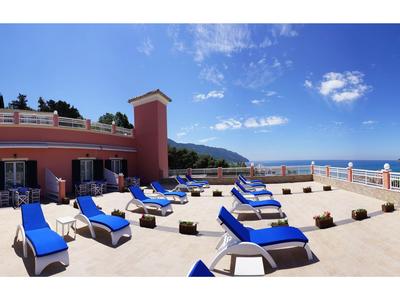 Panorama de una terraza con tumbonas azules y vista al mar bajo un cielo azul.