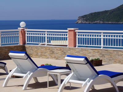Tres tumbonas con cojines azules en una terraza con vistas al mar y una colina costera al fondo