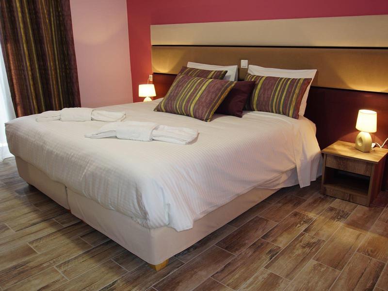 Pohodlná manželská postel s bílým povlečením a polštáři v teplém, moderním hotelovém pokoji.