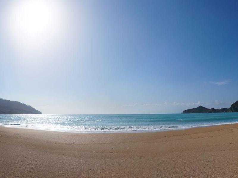 Široká písečná pláž s jasnou oblohou a klidným mořem za slunečního světla