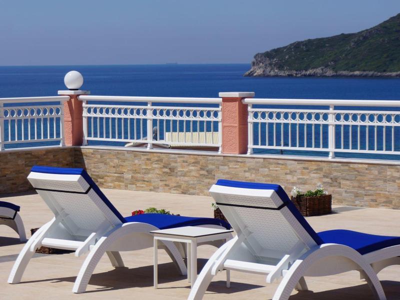 Dva bílé lehátka s modrými polštáři na terase s výhledem na moře.