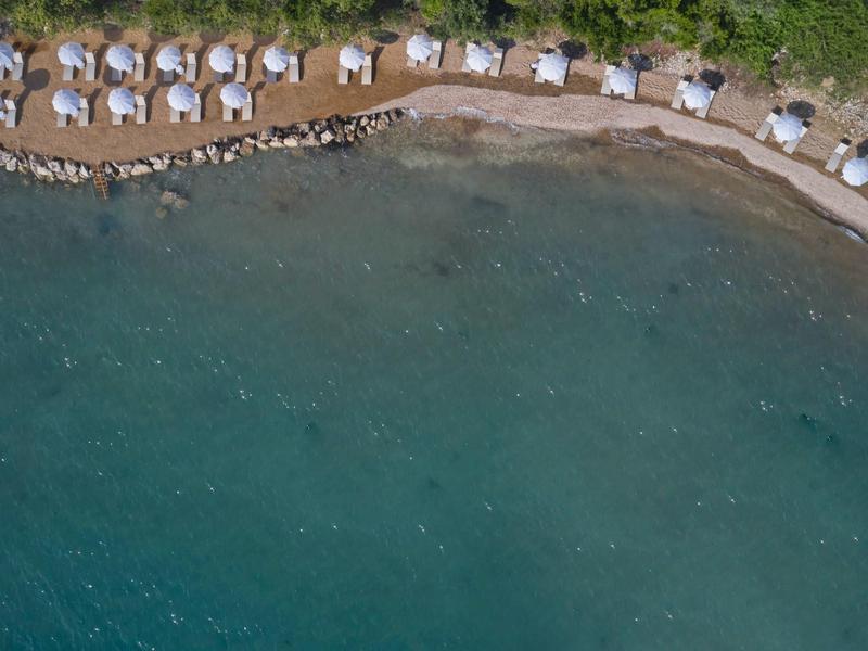 Aerial view of a beach with rows of umbrellas and lounge chairs along the shoreline.