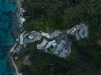 Luftaufnahme eines Resorts mit Pools, umgeben von dichtem Grün und Strand.