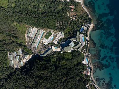 Luftaufnahme eines Resorts am Meer mit mehreren Gebäuden, umgeben von Wäldern und einer felsigen Küste