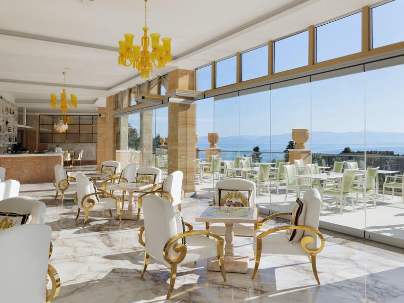 Helles, elegantes Café mit weißen Stühlen, goldenen Akzenten und Meerblick durch große Fenster.