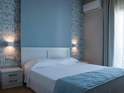 Chambre d'hôtel confortable avec lit double, décoration murale bleue et blanche, accès au balcon.