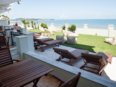 Vue d'une terrasse avec des tables en bois et des chaises longues à côté de la pelouse et de la mer en arrière-plan.