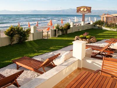 Vista sulla spiaggia con lettini su una terrazza, mare e montagne sullo sfondo.