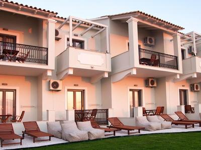 Modernes Hotel mit weißen Wänden, Balkon und Liegestühlen auf einem gepflegten Rasen.