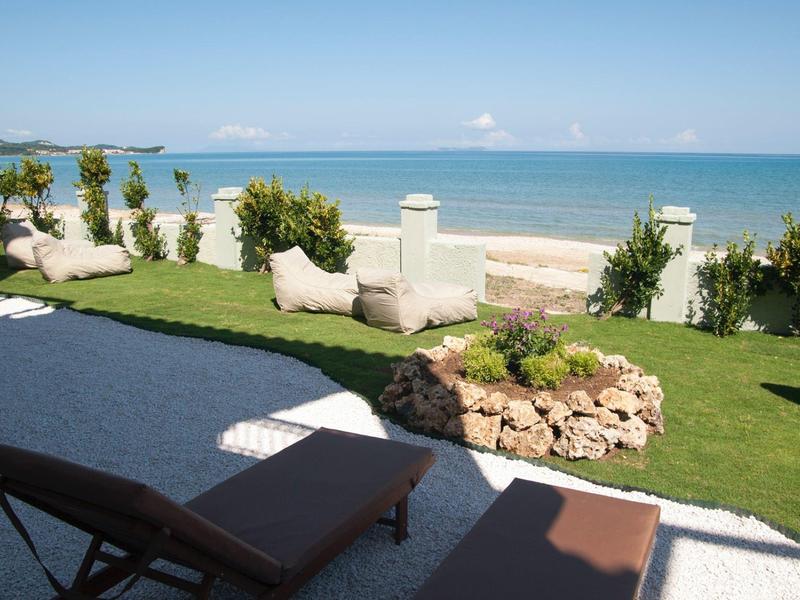 Terrasse ensoleillée avec chaises longues, pelouse verte et vue sur la mer sous un ciel dégagé
