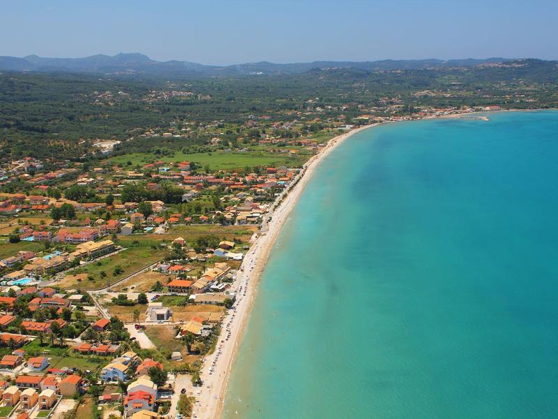Vue aérienne d'une longue plage avec de l'eau turquoise et un paysage environnant.