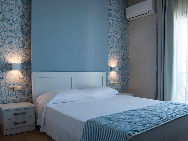Chambre d'hôtel confortable avec lit double, décoration murale bleue et blanche, accès au balcon.