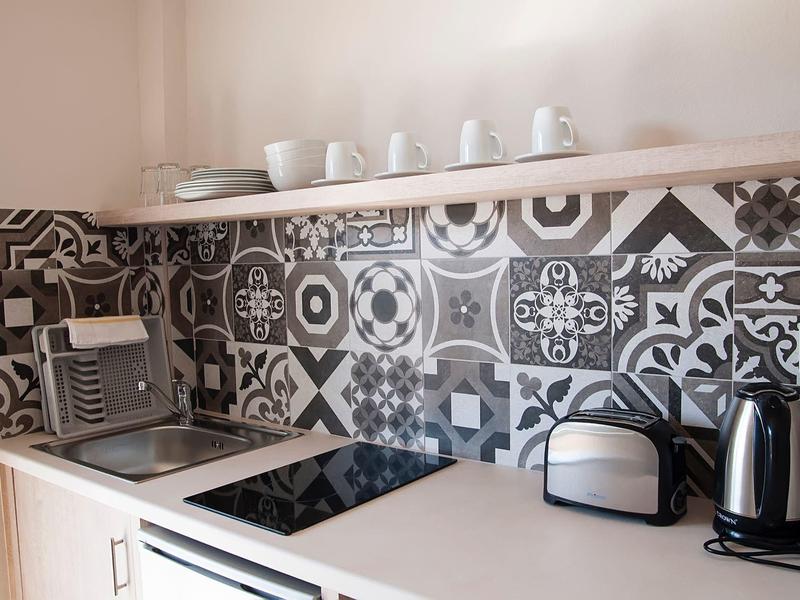 Cuisine moderne avec carreaux à motifs, plaque de cuisson, grille-pain, bouilloire et tasses sur une étagère.