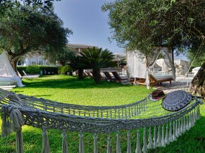 Hängematte zwischen Bäumen auf grünem Gras vor einem Ferienhaus mit Sonnenschirmen.