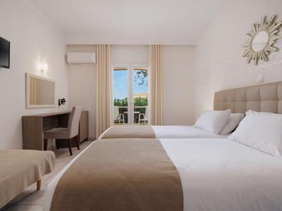Hell eingerichtetes Hotelzimmer mit Doppelbett, Sesseln, Schreibtisch und Balkon mit Blick auf das Meer.