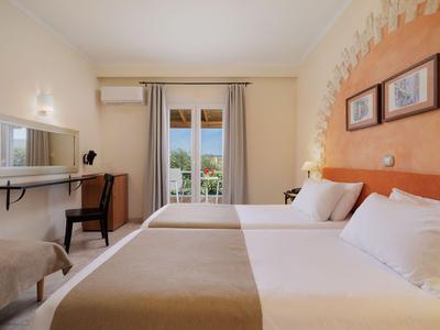 Helles Hotelzimmer mit zwei Betten, Schreibtisch und Balkon mit Blick ins Grüne.