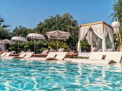 Poolbereich mit Liegestühlen und Sonnenschirmen neben einer geschützten Lounge im Freien bei klarem Himmel.