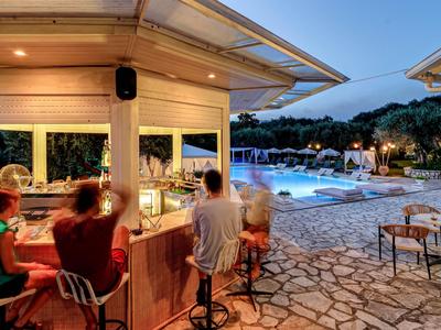 Außenbar mit Gästen neben beleuchtetem Pool und Sitzbereich bei Dämmerung im Hotel.