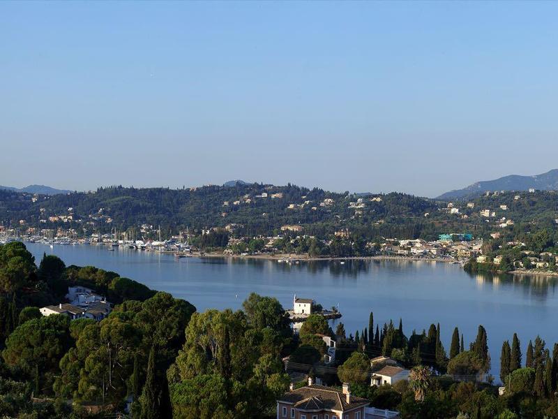 Panoramic view of a lake surrounded by hills and green forests under a clear sky.