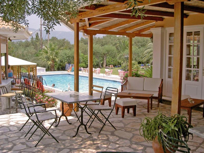 Sunny patio with seating area beside a pool in a green garden.