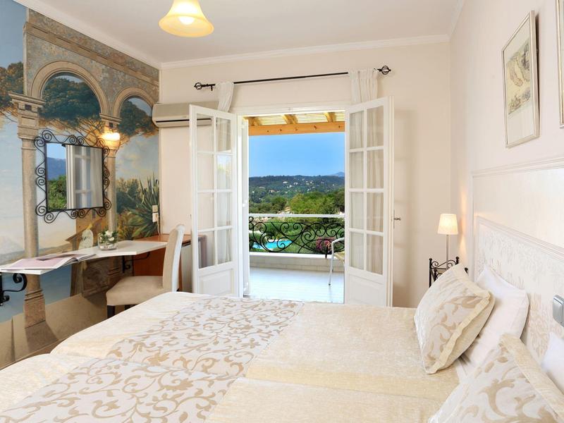 Brightly decorated bedroom with double bed and balcony overlooking the sea and green landscape.