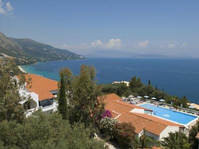 Zeezicht met bergen, rode daken, bomen en een zwembad onder een heldere hemel